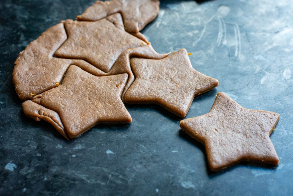 Cutting rolled out gingerbread cookie dough with star-shaped cookie cutter. 