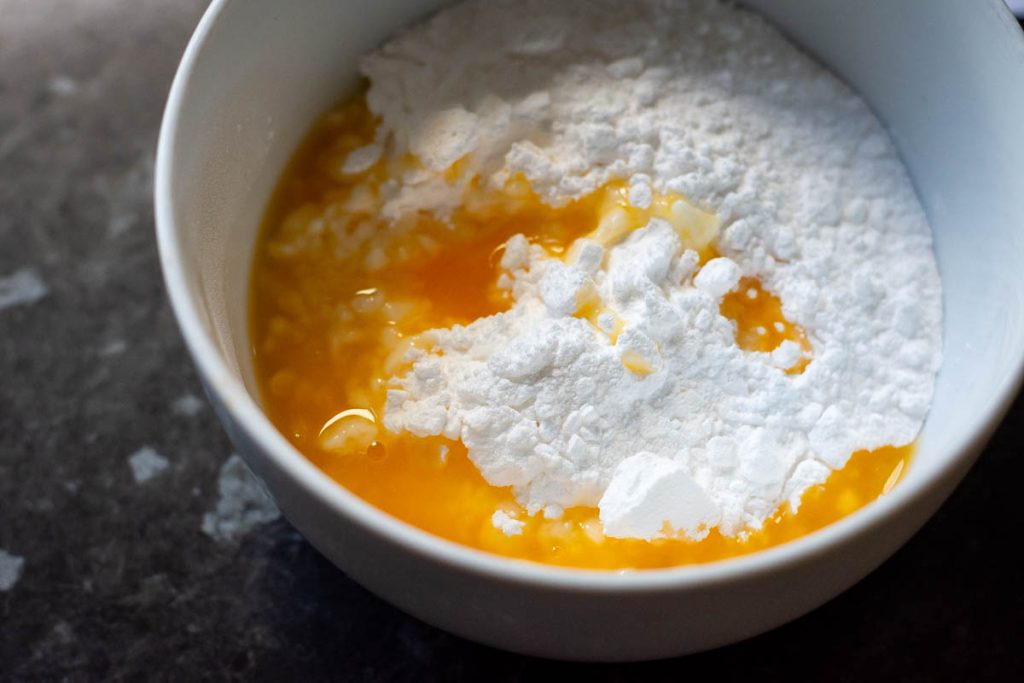 Icing sugar and orange juice in a white bowl. 