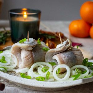 Two pieces of Lithuanian Pickled Herring Rollmops with onions at the base on a Christmas Eve Table.