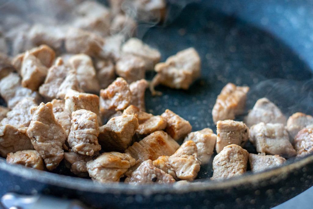 Pork cubes searing in a pan.