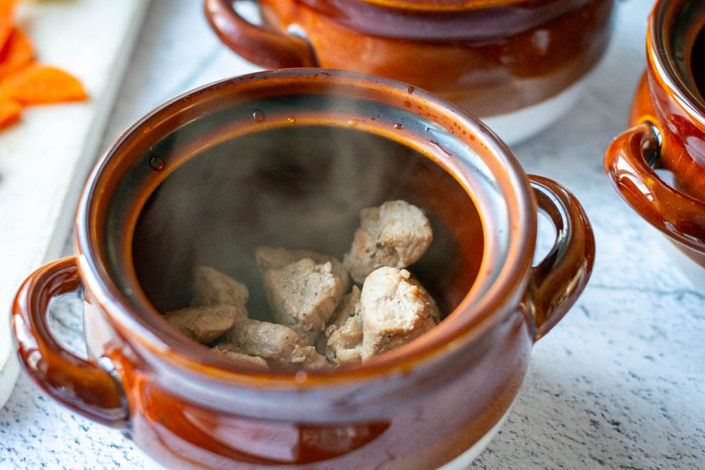 Seared pork cubes at the bottom of the clay pot steaming.