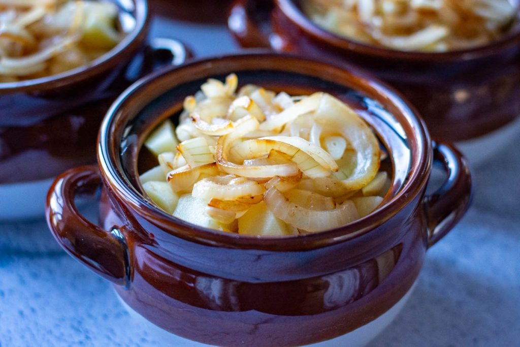 Onions and garlic on top of potatoes in a clay pot.