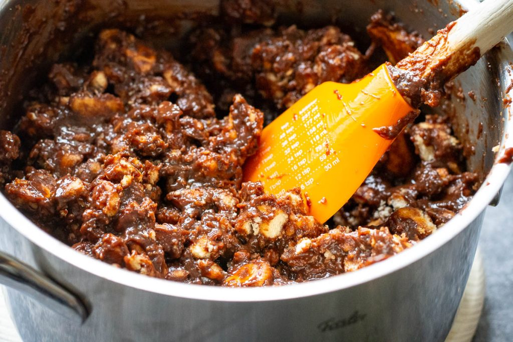 Cookies coated in chocolate mixture with an orange rubber spatula in it.