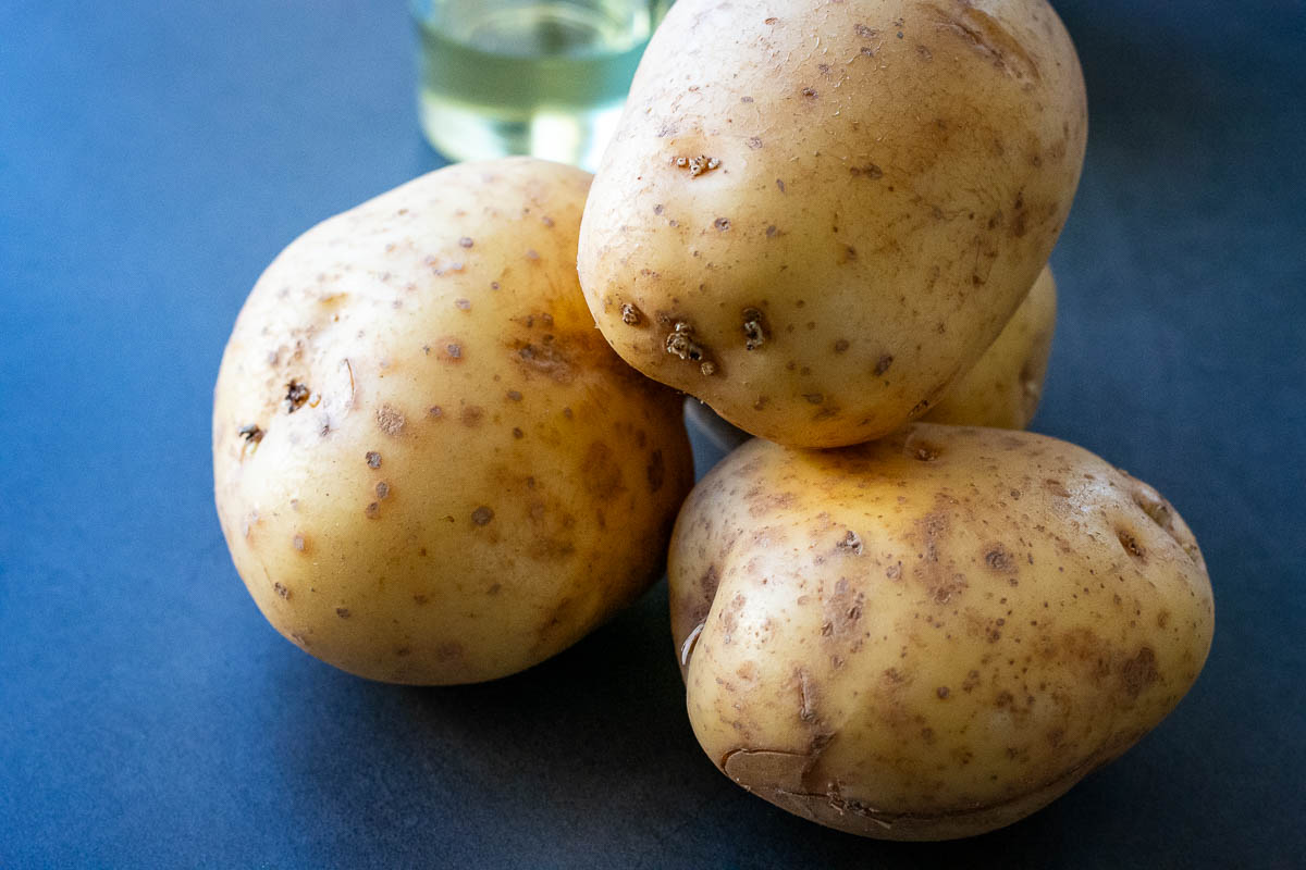 Starchy potatoes unpeeled on a dark surface.