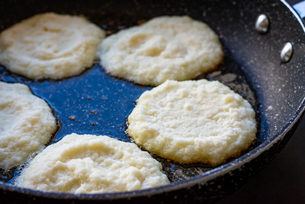 5 Lithuanian potato pancakes frying in a pan on their first side.