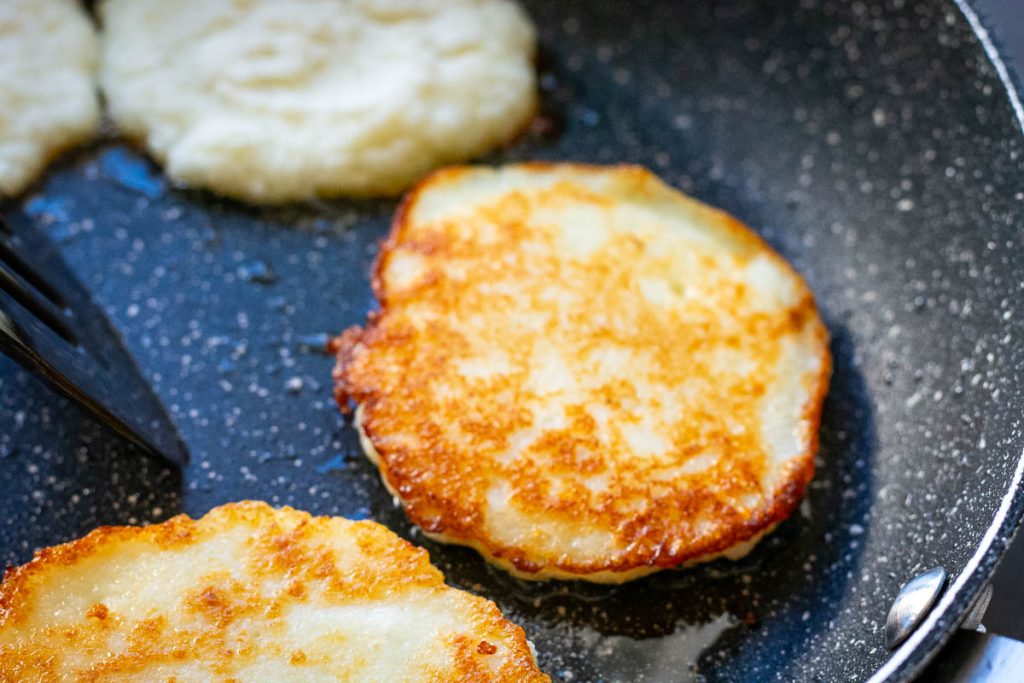 Flipped potato pancakes showinf golden brown crispy side in a frying pan.