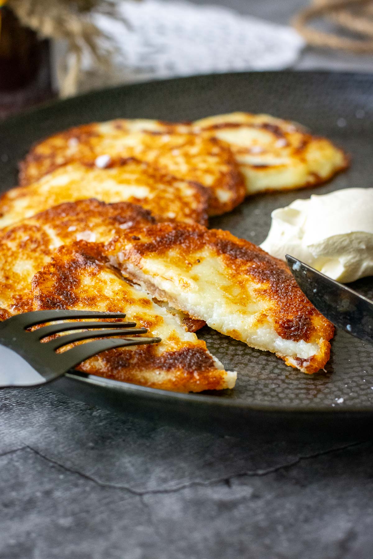 LIthuanian potato pancakes on a black plate with one pancake being cut in half.