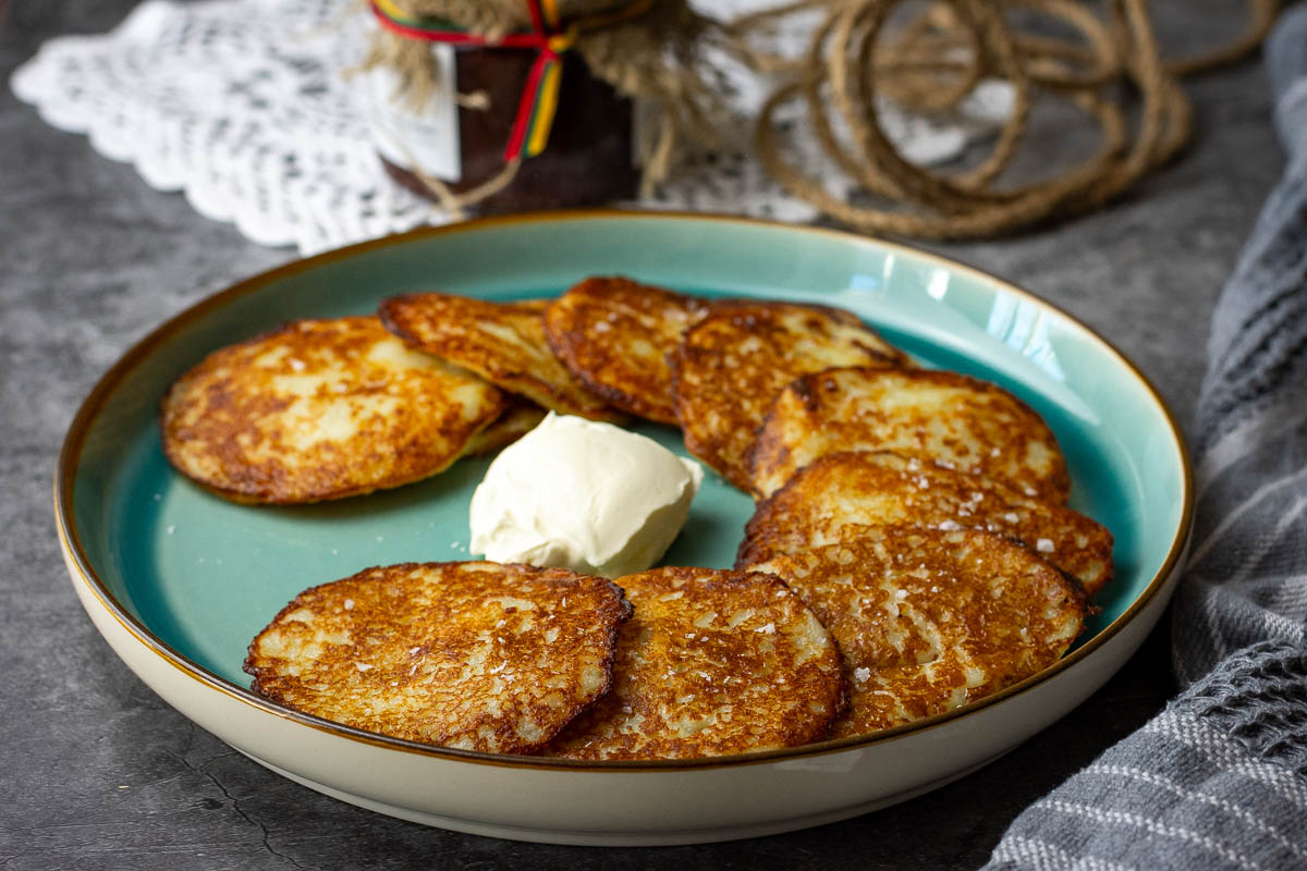 Lithuanian potato pancakes arranged in a semi-circle on a teal colored plate with sour cream in the middle.