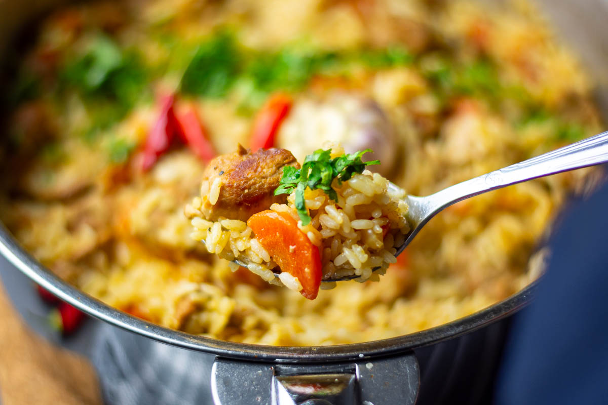 A spoonful of pork pilaf lifted out of the pan.