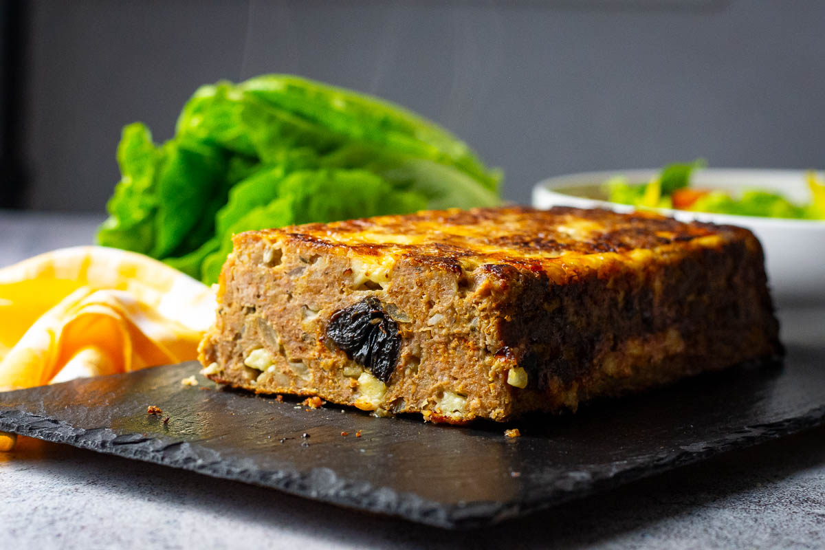 Lithuanian meatloaf with prunes in the centre on a black slate board.