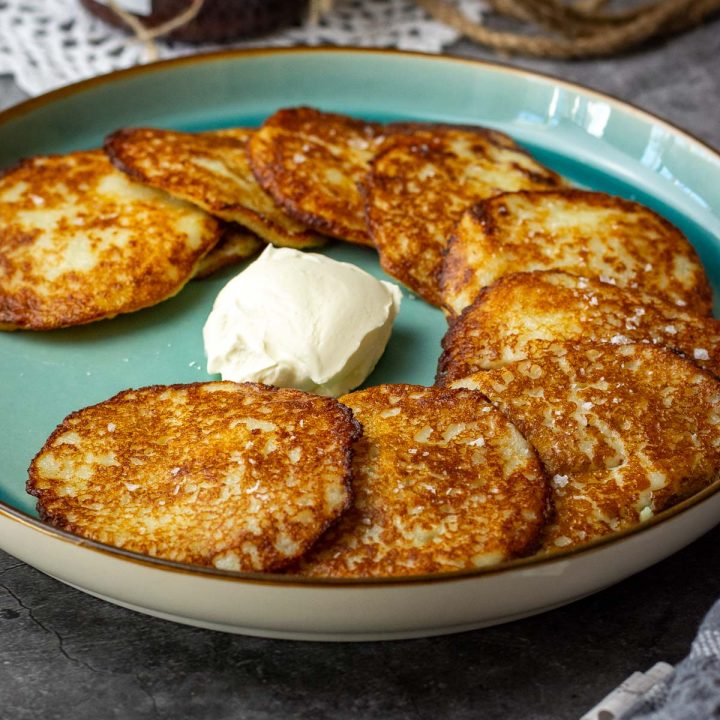 Lithuanian potato pancakes arranged in a semi-circle on a teal colored plate with sour cream in the middle.