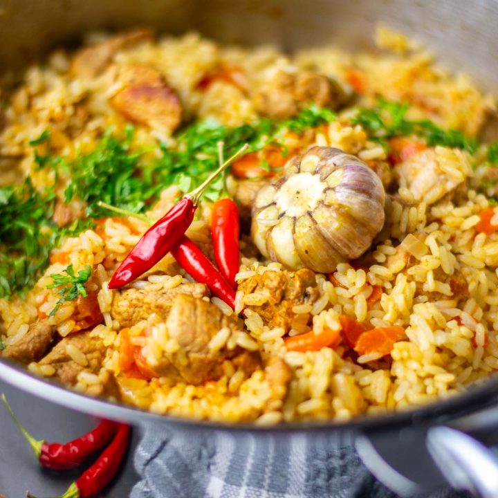 Lithuanian Pork Plov in a pan with a bulb of garlic in the middle.