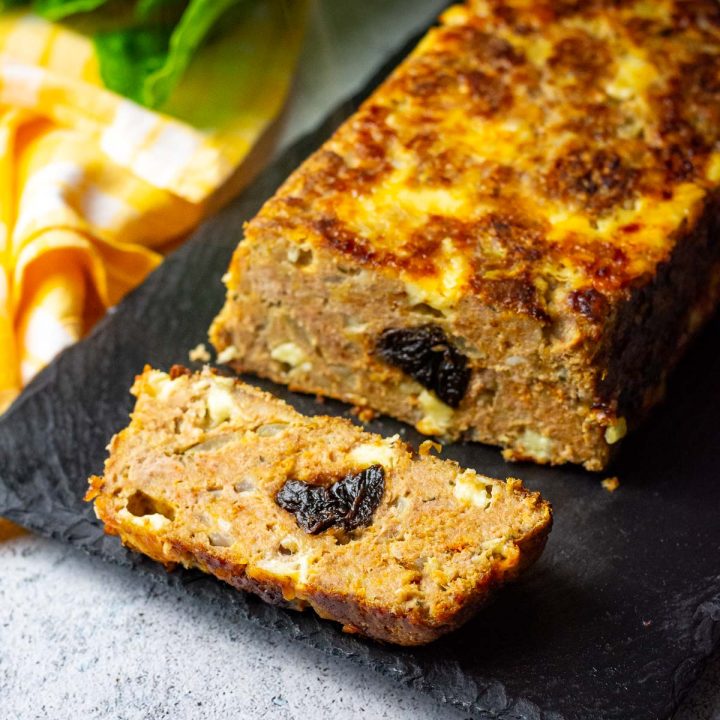 LIthuanian Cheesy Turkey Meatloaf With Prunes in the middle on a black board with one slice cut.