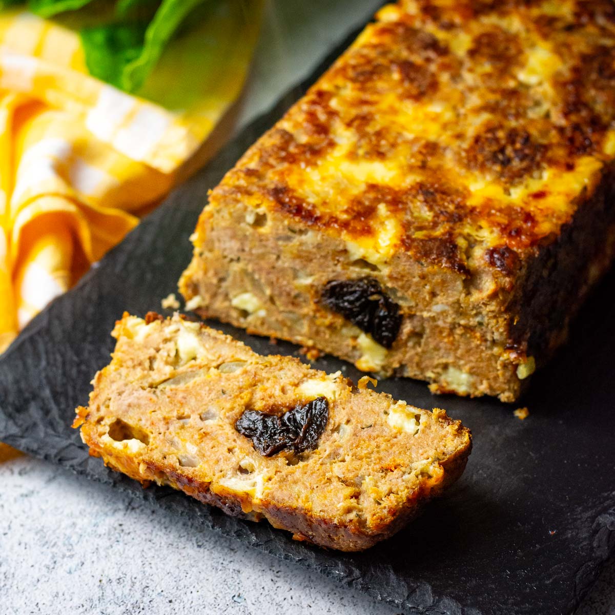 LIthuanian Cheesy Turkey Meatloaf With Prunes in the middle on a black board with one slice cut.