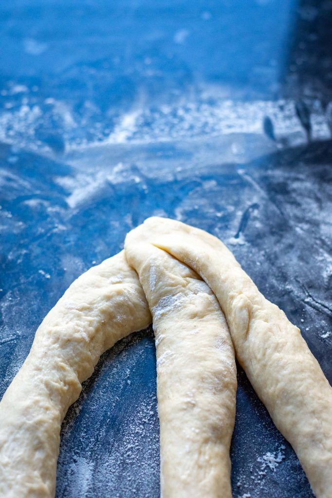 Three dough ropes attached at one end on a floured surface. 
