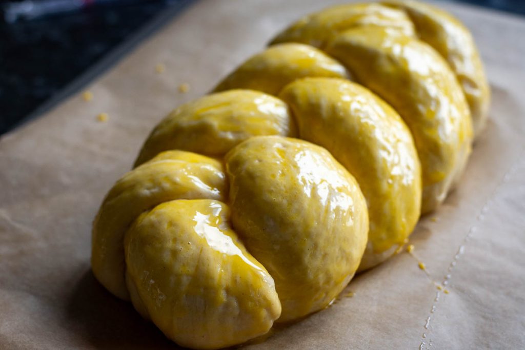 Eggwashed Lithuanian braided bread on a parchment lined baking sheet. 