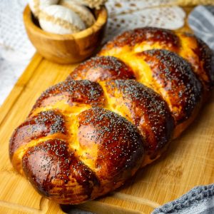 Dark Golden Brown Lithuanian Easter Bread (a.k.a. Mieline Pyne) on a large chopping board with a bread knife next to it.