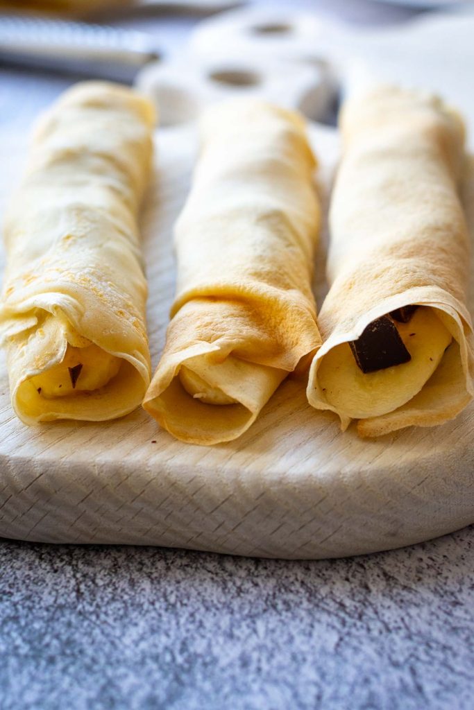 Three banana crepes on a wooden board.