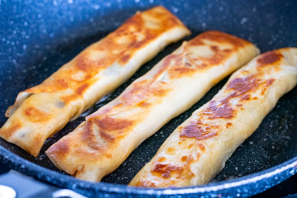 Banana crepes turning golden brown in the pan.