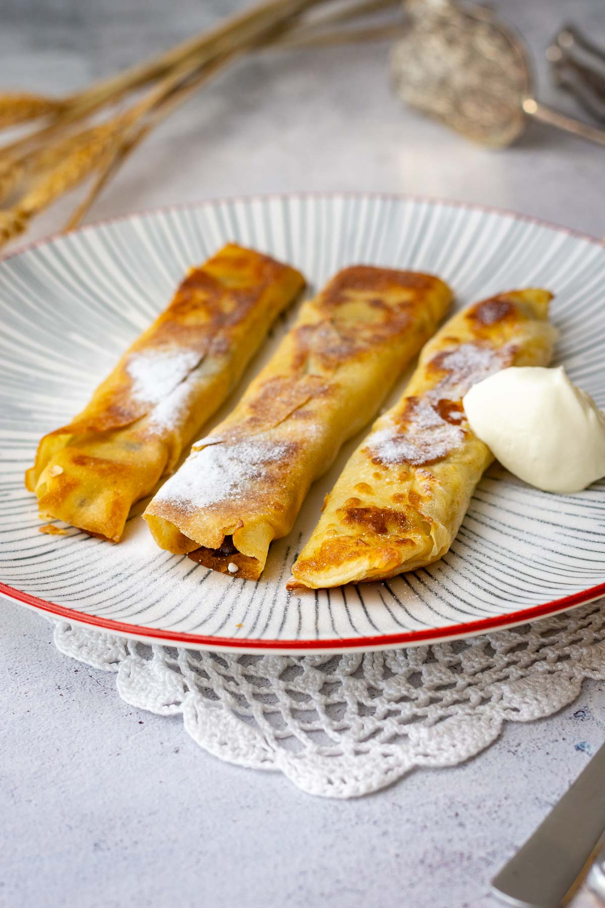 Lithuanian crepes with bananas served with a dollop of sour cream and powdered sugar on top.