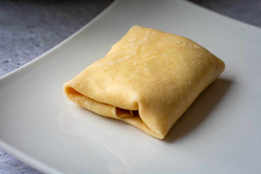 Crepe is shaped and placed on a white plate, ready for frying.