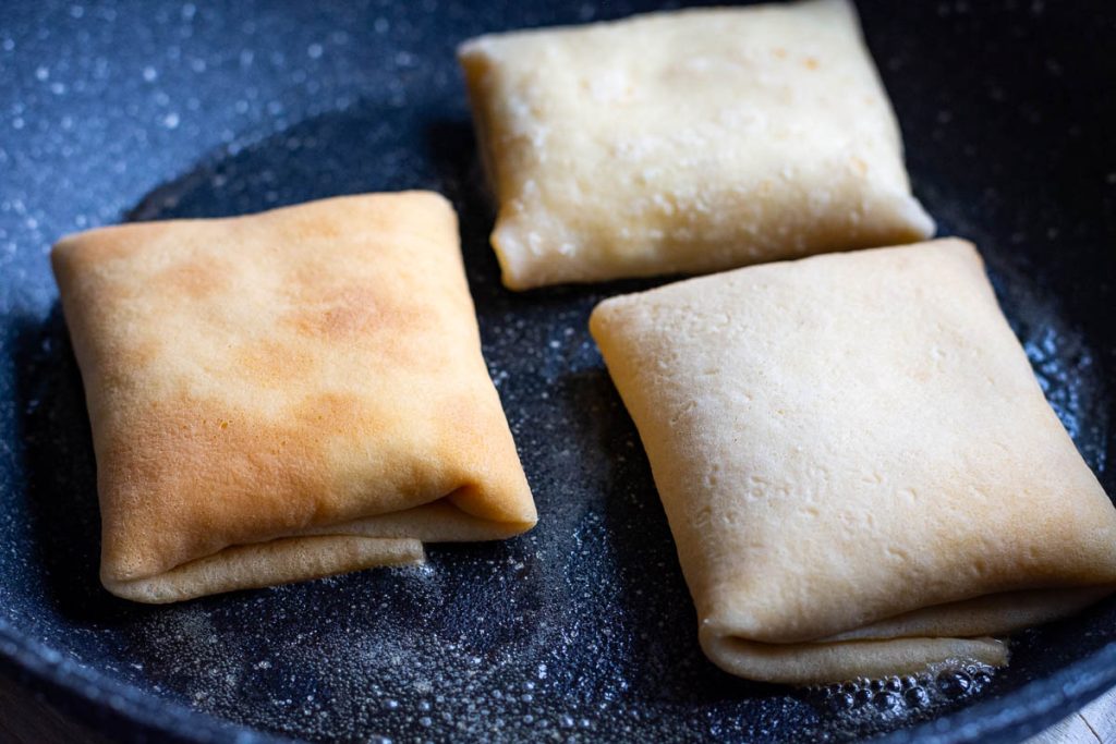 Three farmer's cheese crepes in a frying pan.