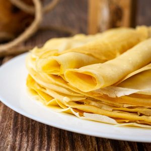 Lithuanian Crepes stacked on a plate with the top two rolled into tubes.