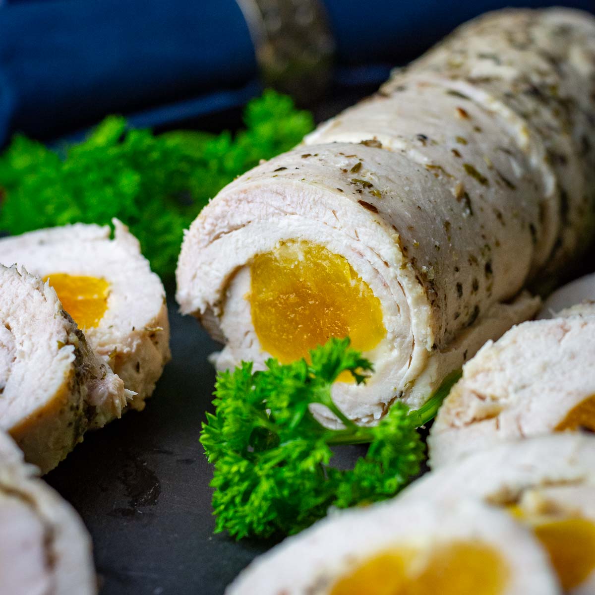 Lithuanian Chicken roulade with aprocot filling on a black slate board garnished with parsley.