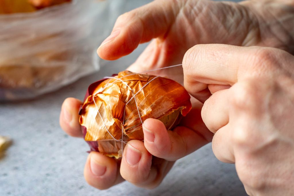 Egg wrapped in onion skins that are being secured with a thread. 
