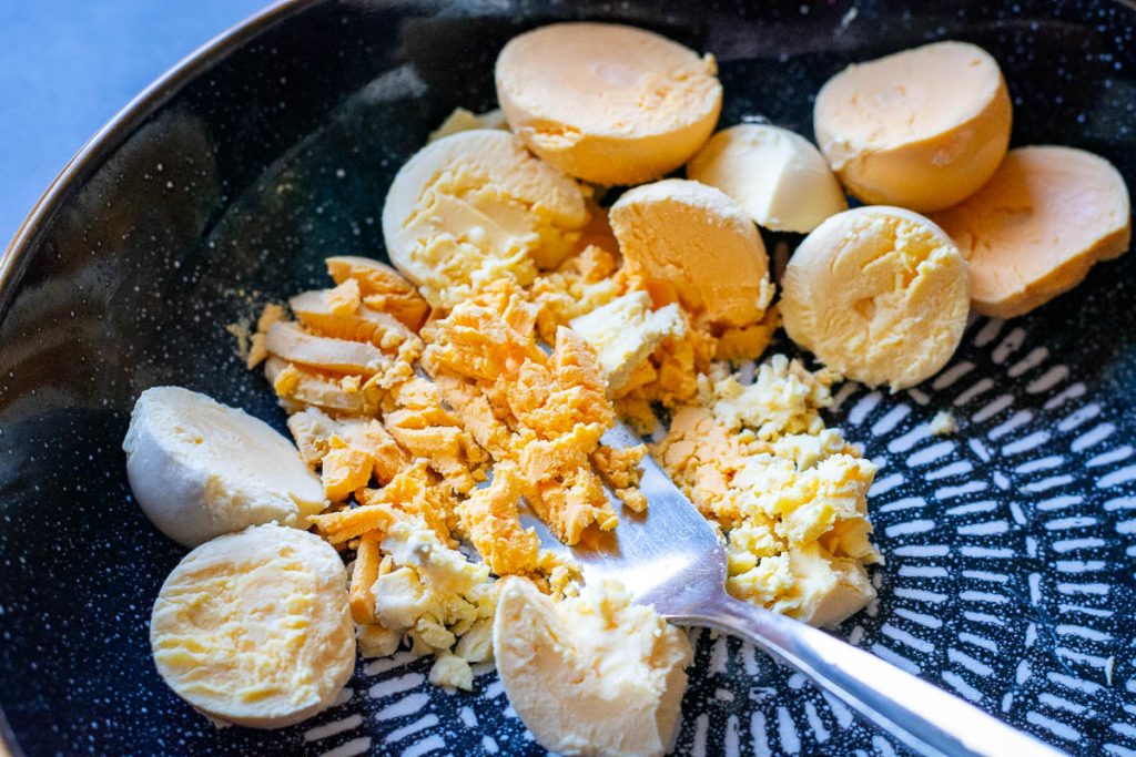 Mashing the egg yolks with a fork in a bowl.