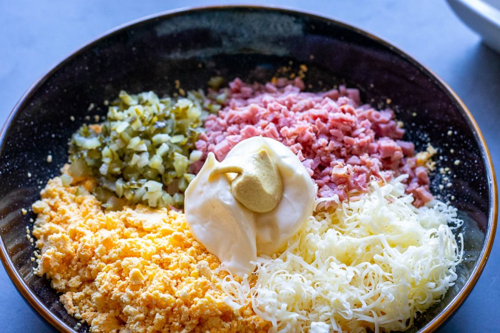 All ham and cheese deviled egg filling ingredients in a bowl unmixed.