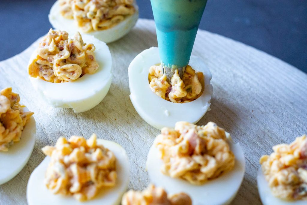 Piping the ham and cheese deviled egg filling into egg whites.