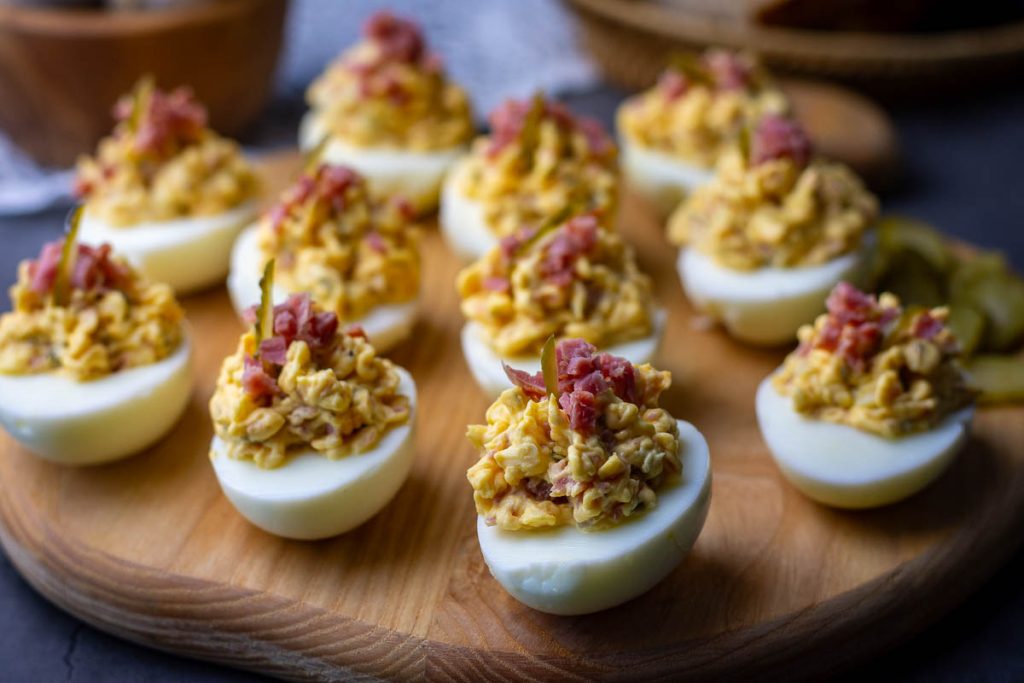 Lithuanian deviled eggs with ham and cheese decortaed with finely diced ham on a wooden board.