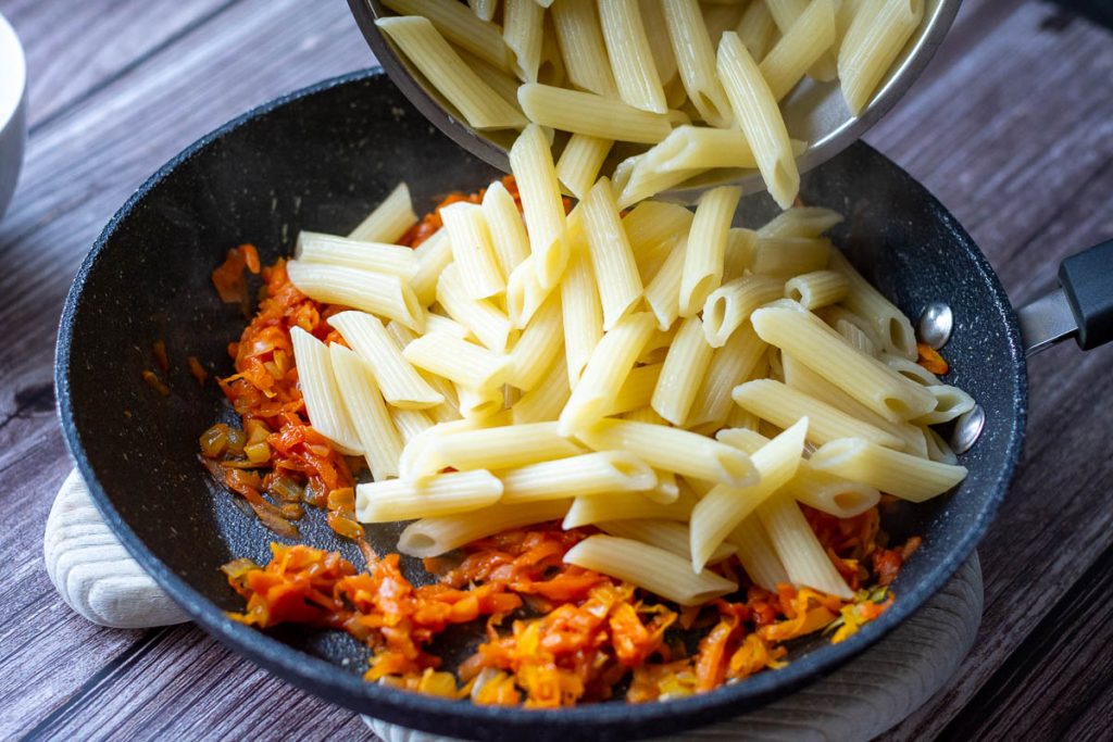 Adding cooked drained penne pasta to the sauteed vegetable mixture.