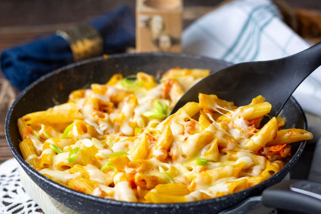 Taking a spoonful of cheesy pasta with carrots and onions from the pan.
