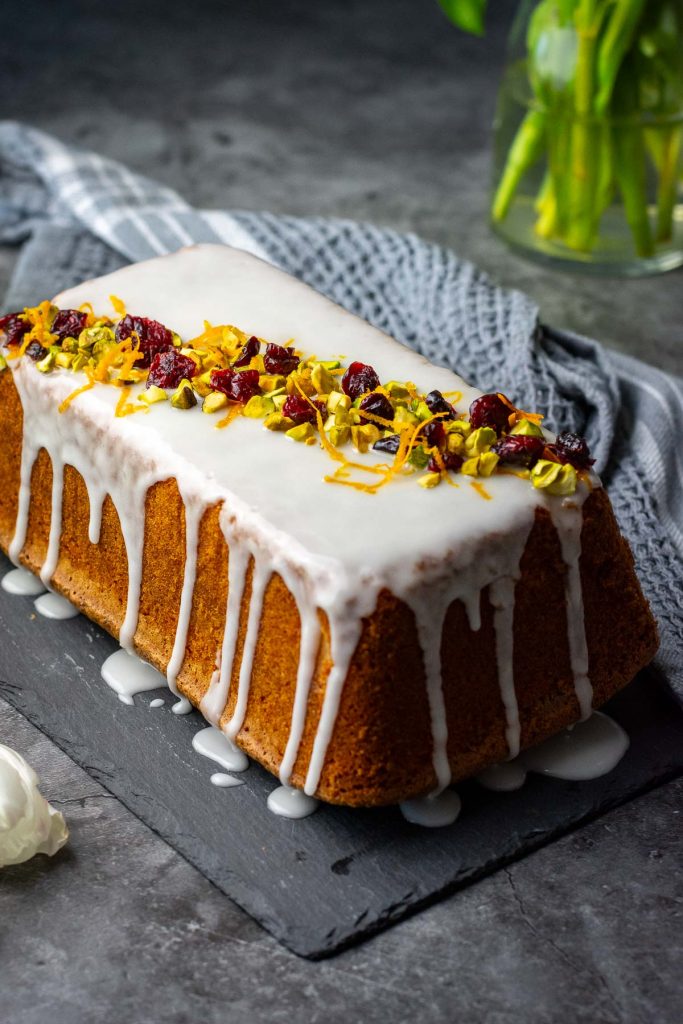 Lithuanian orange loaf cake decorated with dried cranberries and chopped pistachio nuts. 