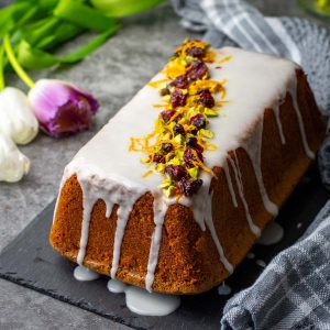 Lithuanian orange loaf cake with icing glaze decorated with cranberries, pistachios and orange zest.