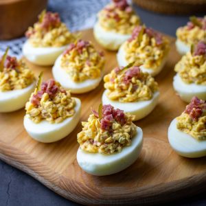 Lithuanian deviled eggs with ham and cheese on a wooden board.