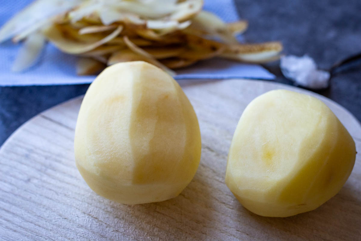 Two peeled potatoes on a wooden cutting board. 