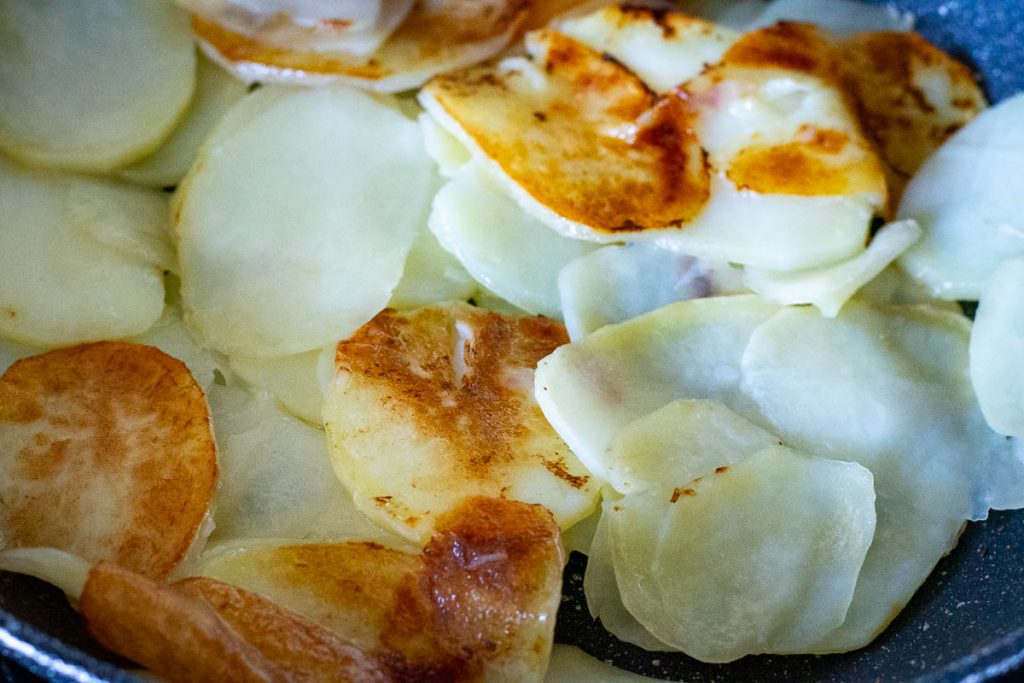 Potatoes being flipped in a frying pan. 