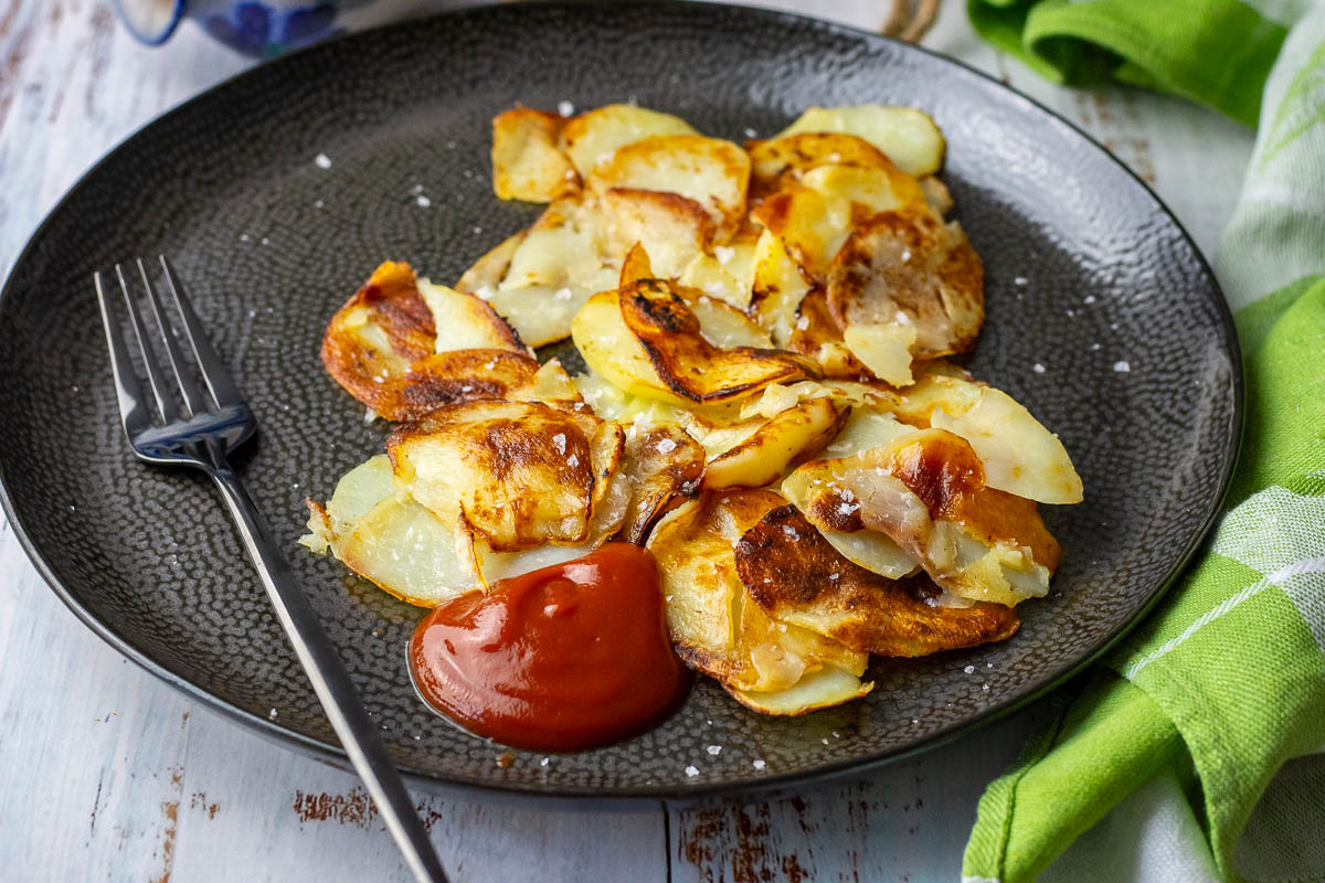 Lithuanian Pan Fried Sliced Potatoes With Ketchup in a black plate.