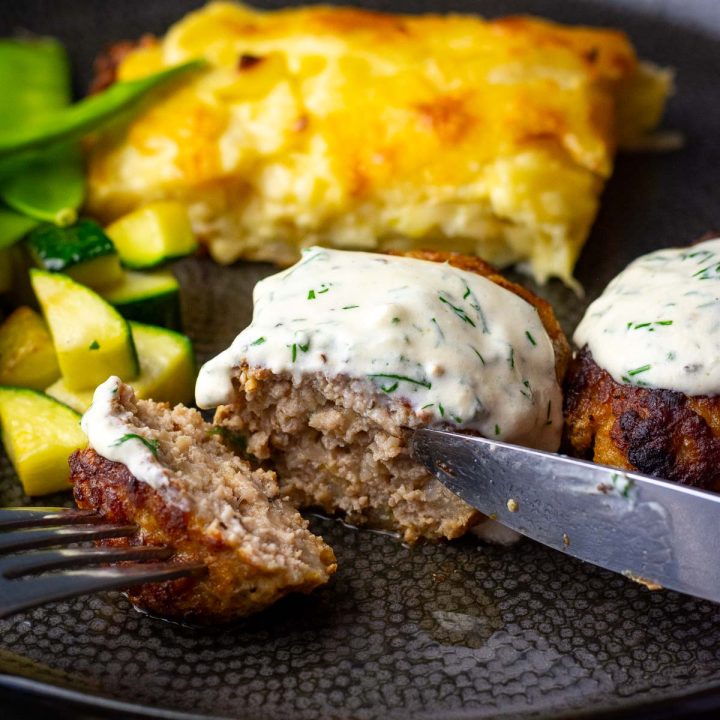 Lithuanian meatball with sour cream sauce on top on a black plate.