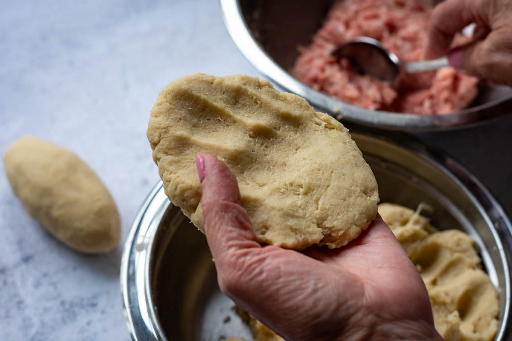 A piece of potato dough flattened into a patty in the palm of a hand.