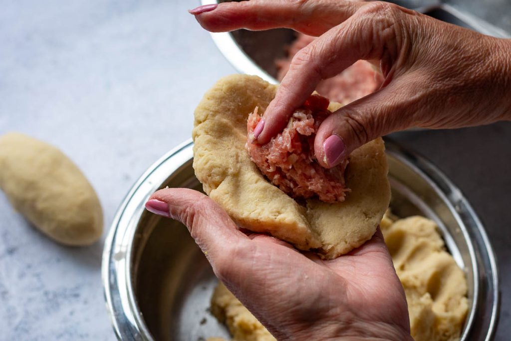 Adding pork filling to the centre of the flattened potato dough.