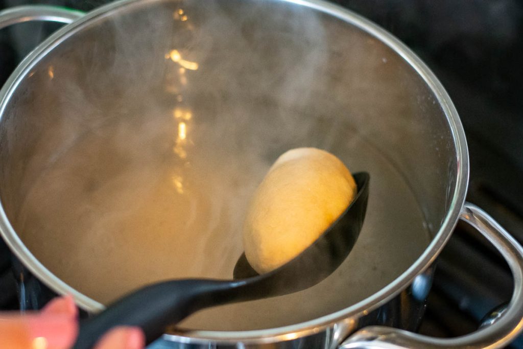 Lowering one meat stuffed potato dumpling into boiling water.