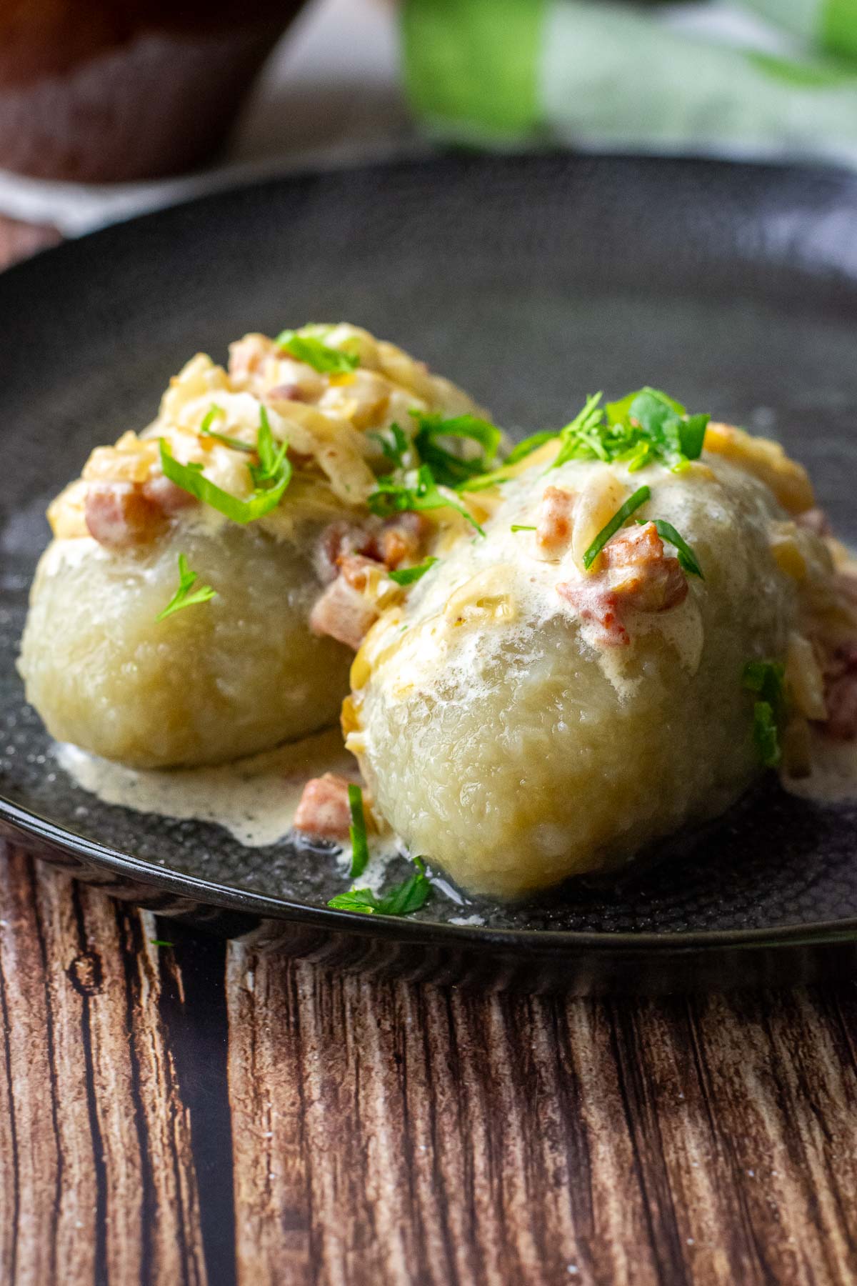Two Lithuanian Potato and meat dumplings with sour cream, bacon and onion sauce on a black plate on a wooden table.