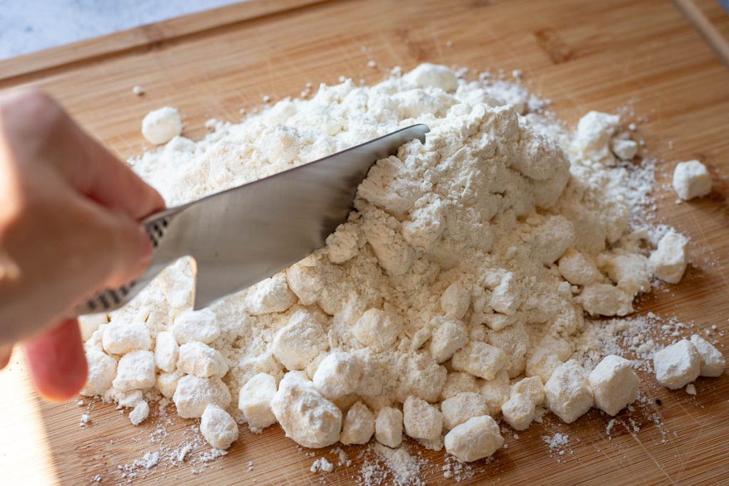 Cutting the cold butter into the flour mixture on a wooden board with a large knife.