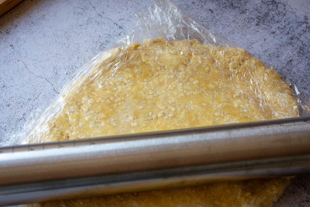 Farmer's cheese cookie dough wrapped into plastic wrap being flattened into a disc.