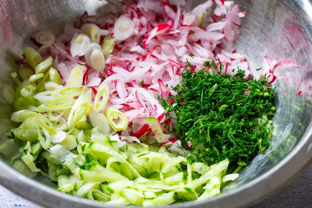 Grated vegetables and chopped herbs in a large mixing bowl.