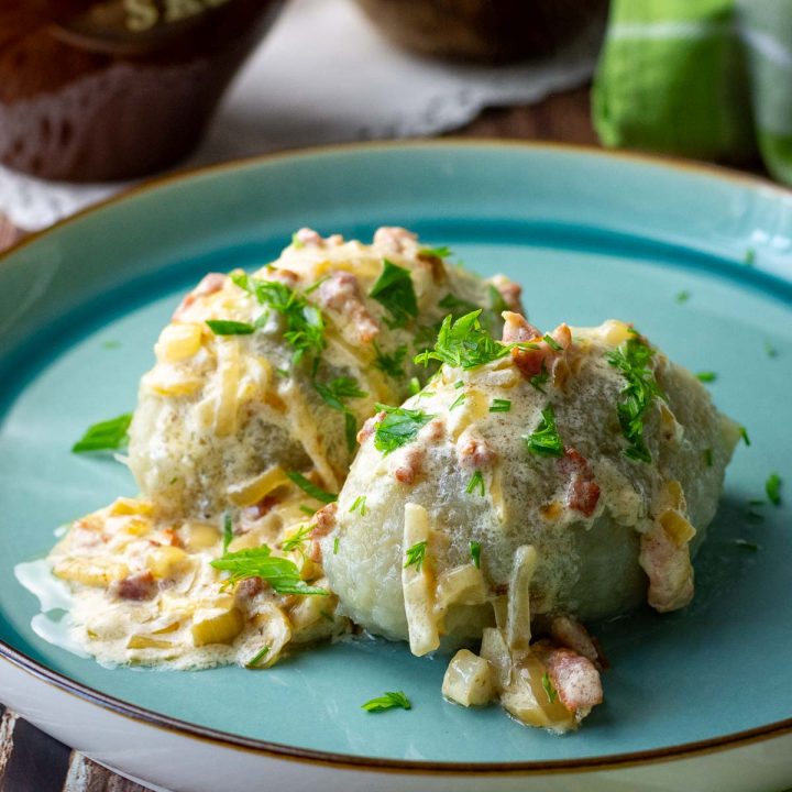Cepelinai (Meat Stuffed Lithuanian Potato Dunplings) on a teal-colored plate with onion and bacon sauce.